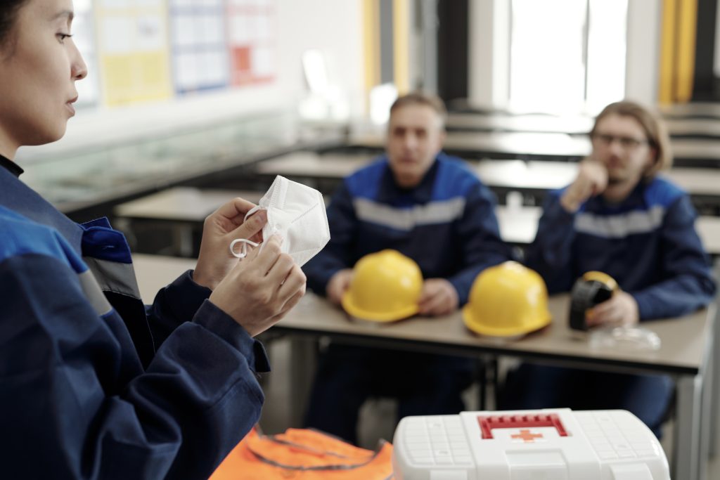 Young woman demonstrating usage of protective mask while standing in front of colleagues in classroom during basics of life safety lesson